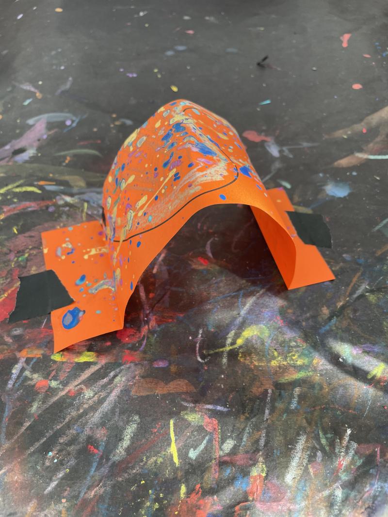 Orange strip of paper with two folded ends, pushed together to create a rounded arch.