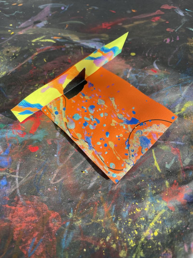 Orange paper, paint splattered, connected at a 90-degree angle with tape.