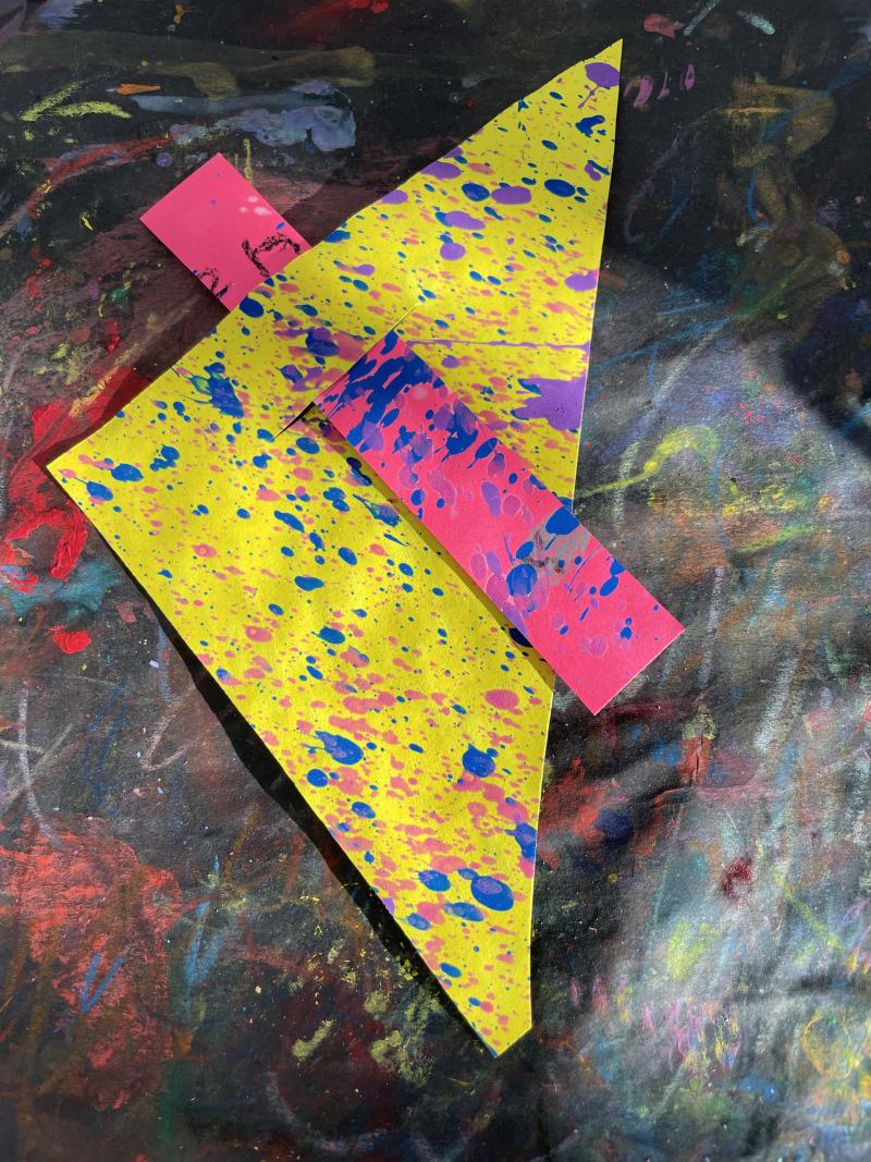 Yellow triangle piece of paper with a pink strip of paper threaded through a slit in the yellow paper.