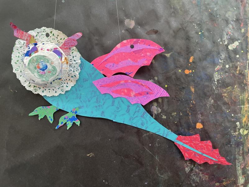 Paper objects and collage papers pieced together to create a colorful dragon puppet.