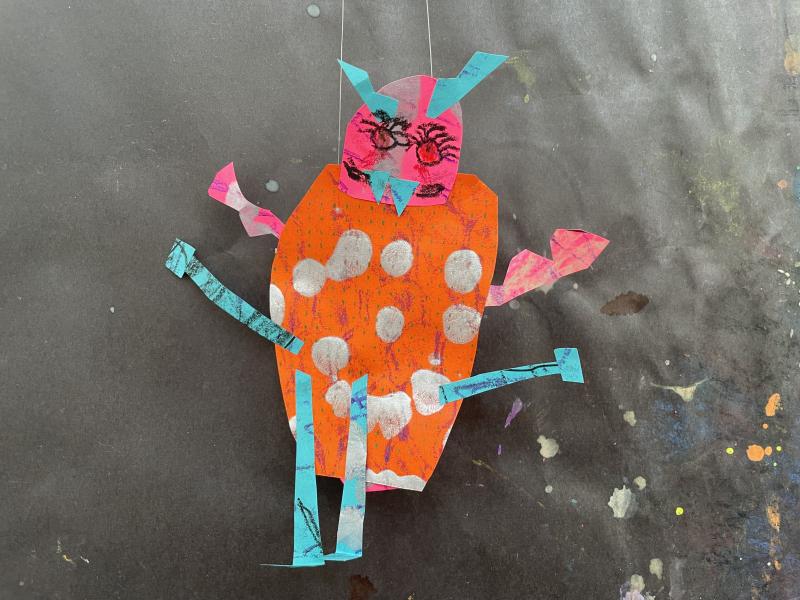 Paper objects and collage papers pieced together to create a colorful dragon puppet.