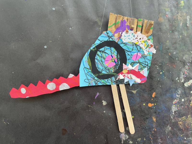 Paper objects and collage papers pieced together to create a colorful dragon puppet.