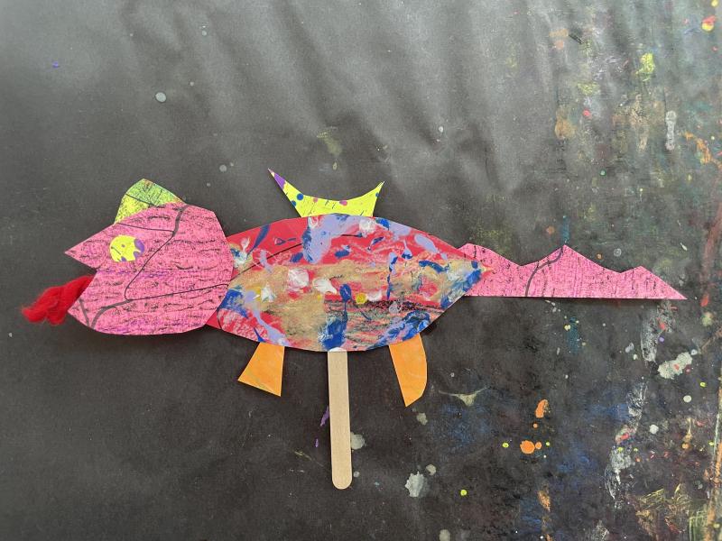 Paper objects and collage papers pieced together to create a colorful dragon puppet.