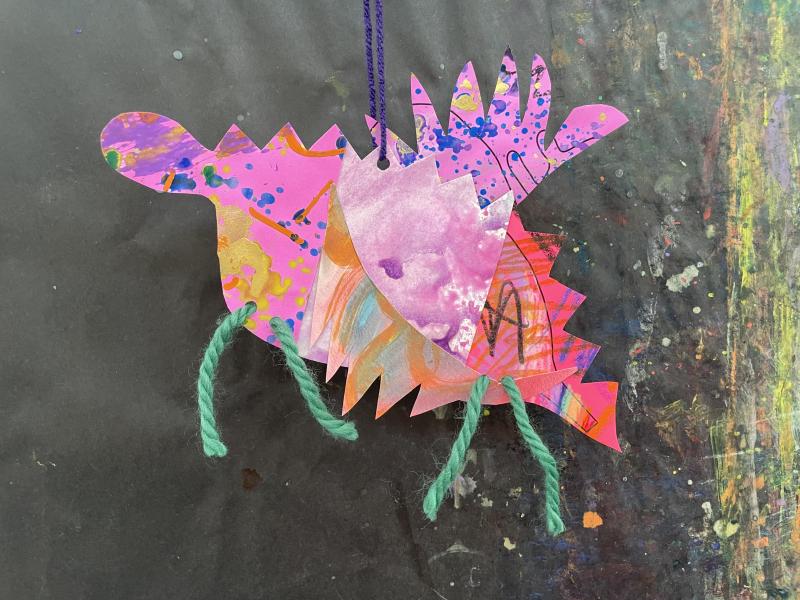 Paper objects and collage papers pieced together to create a colorful dragon puppet.