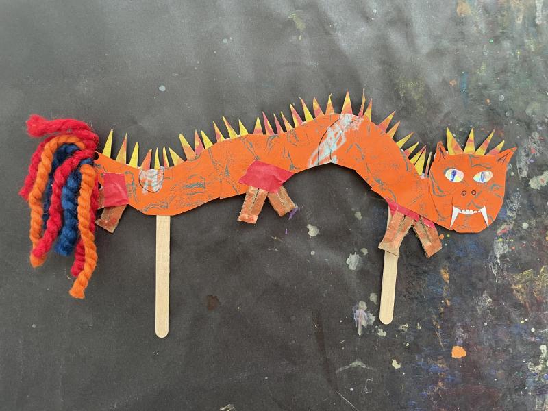 Paper objects and collage papers pieced together to create a colorful dragon puppet.