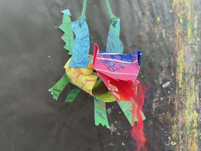 Paper objects and collage papers pieced together to create a colorful dragon puppet.