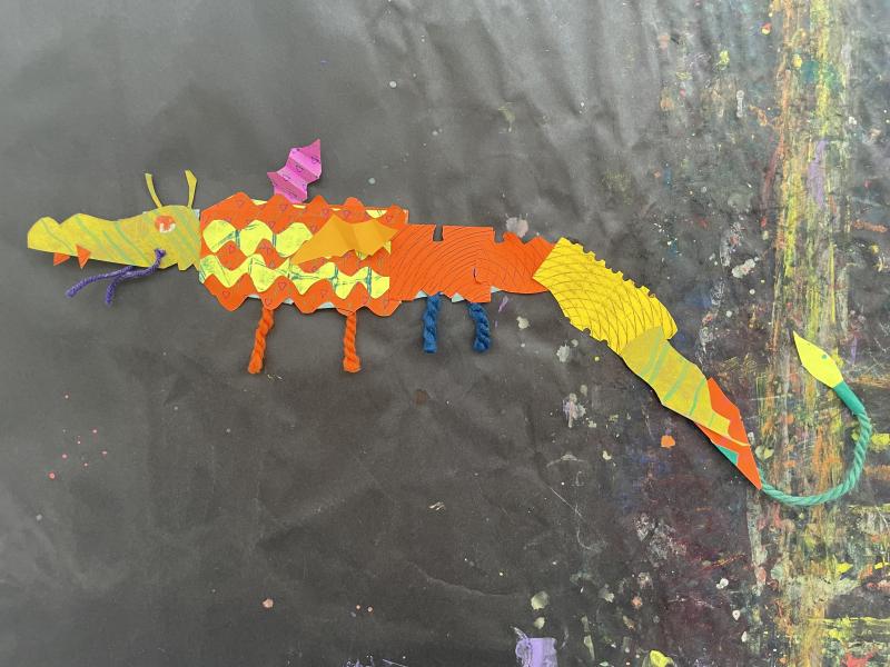 Paper objects and collage papers pieced together to create a colorful dragon puppet.