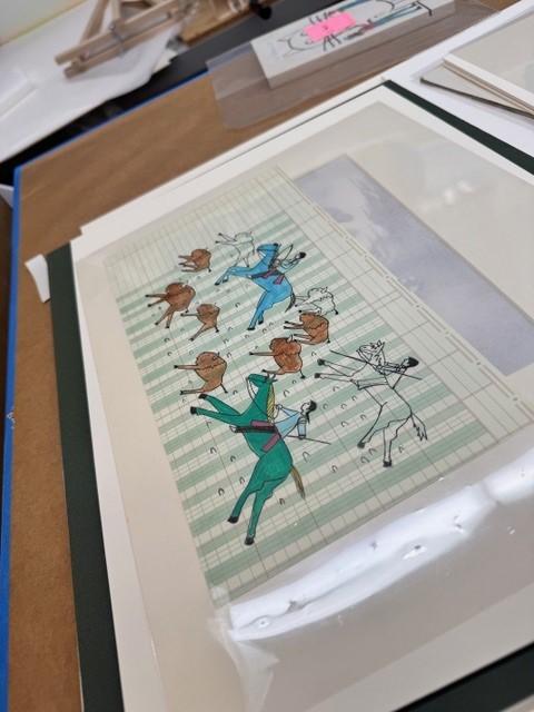 art depicting three people on horseback and buffalo drawn on ledged paper and displayed on a table with other sheets of paper under it