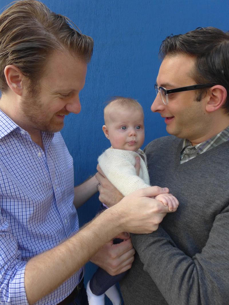 Photograph of two dads holding baby.
