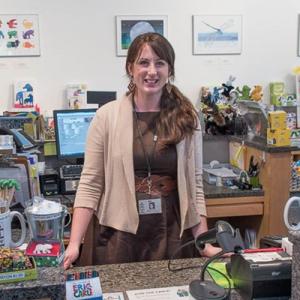 Photograph of Carle Bookshop Manger Eliza Brown standing behind cash register and smiling.
