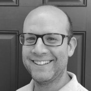 a white man in a white shirt and glasses, smiling