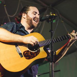 Ryan Hollander playing guitar at a microphone and singing. 