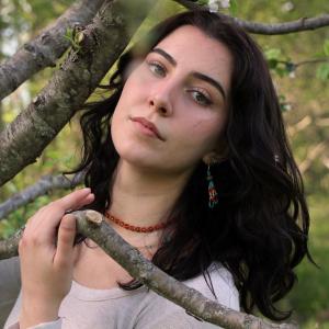Face of young woman with brown hair next to tree