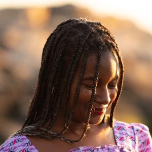 A black woman smiling, wearing a purple patterned dress