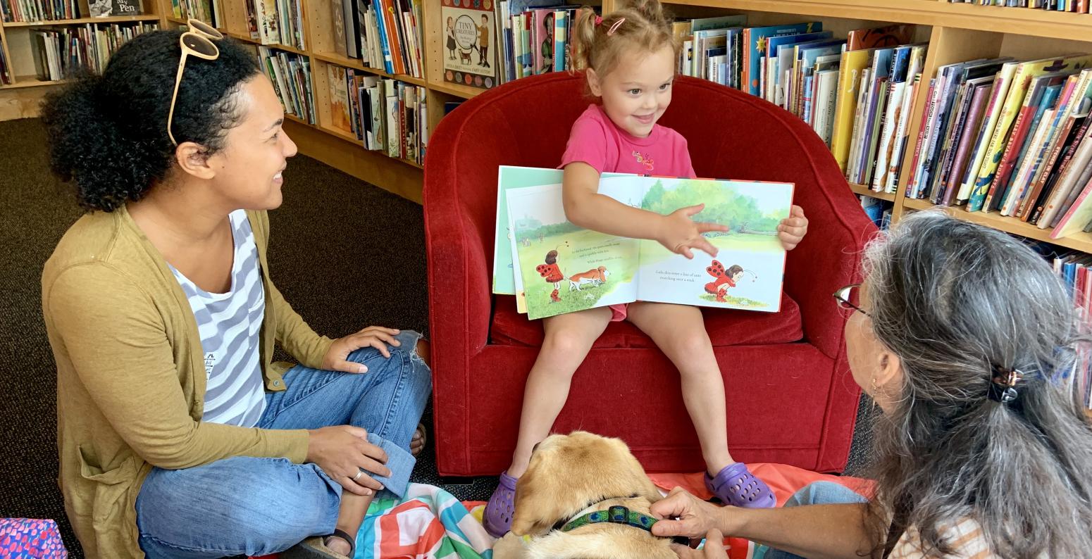 Child sitting in chair showing picture book to reading buddy dog.