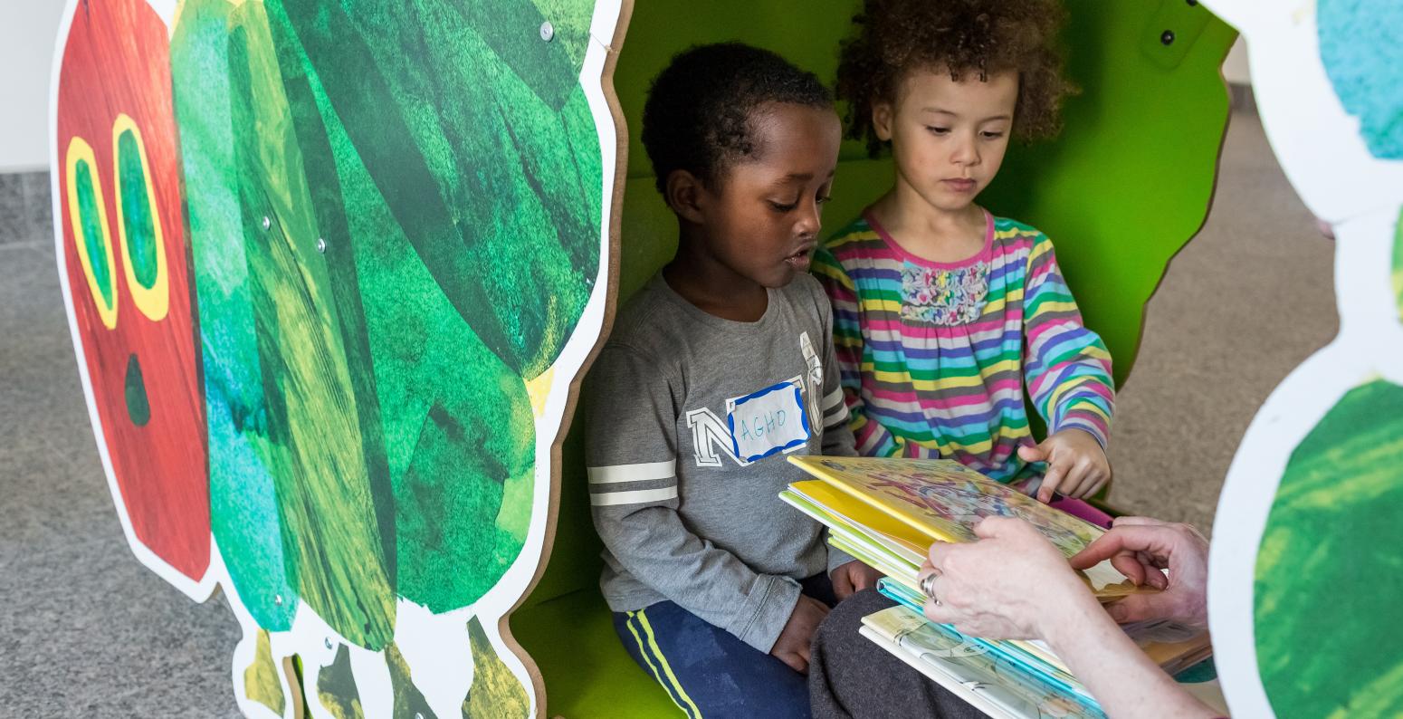 Two children sit in the Caterpillar Cubby with a book.