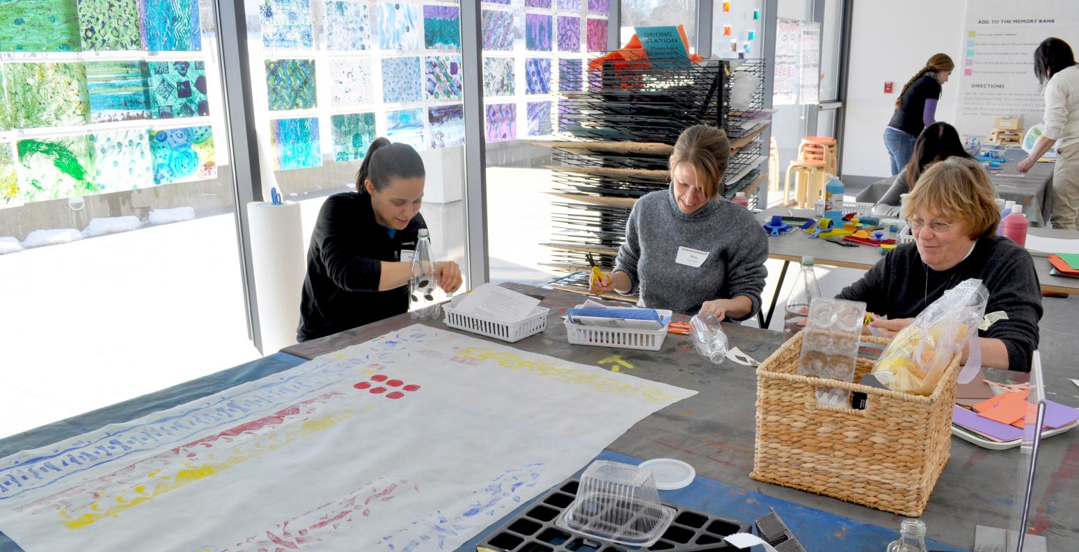 Three educators sitting and printmaking at a large table in the Art Studio.