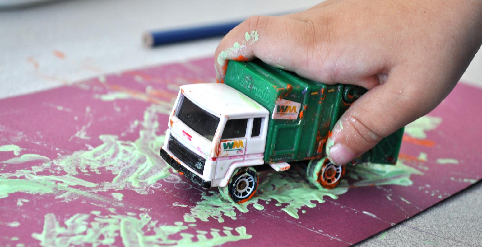 Photograph of child painting with toy truck.