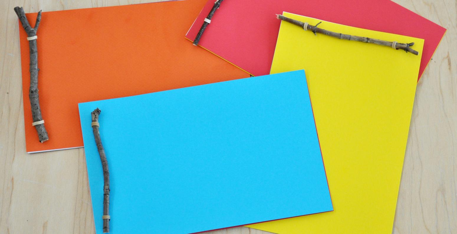 A pile of four brightly colored books bound with sticks and rubber bands.