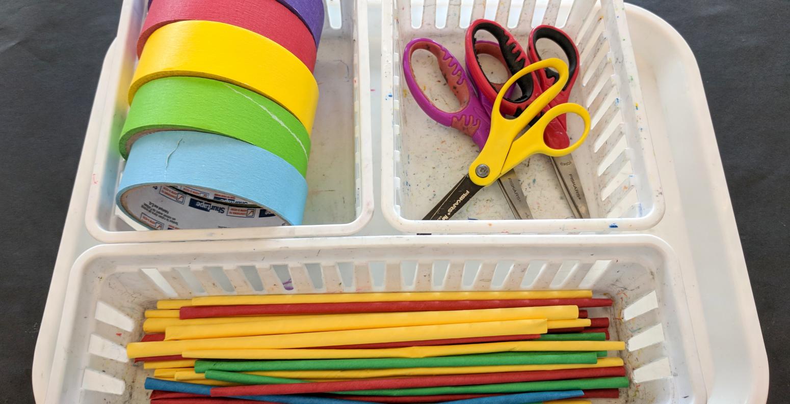 Baskets on a tray filled with colorful tape, straws, and scissors.