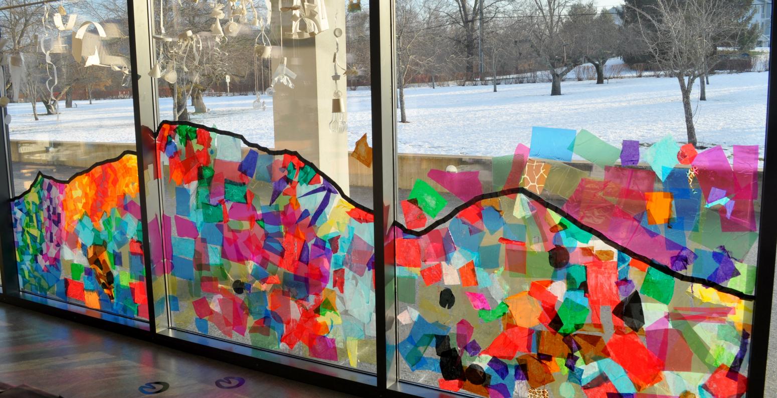A colorful tissue-paper-collage mountain across three panels of windows.