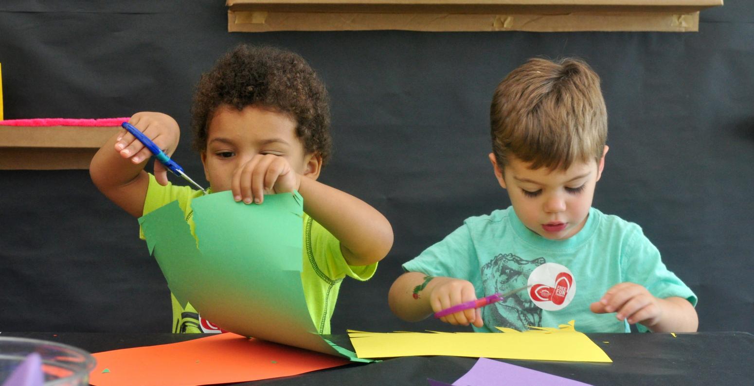 Two young children cutting colorful construction paper at a table.