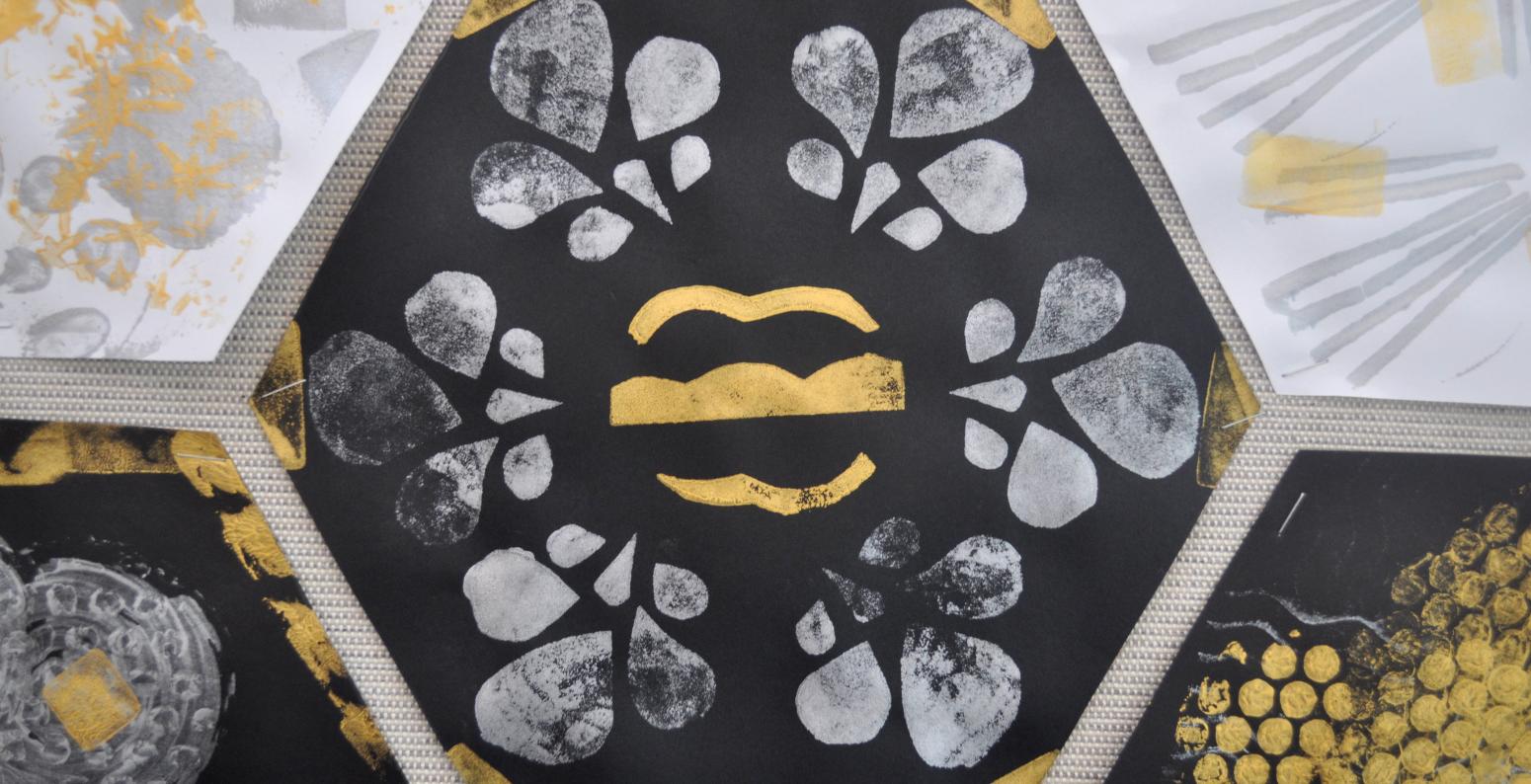 A hexagon-shaped piece of black construction paper with gold and silver stamped shapes on it.
