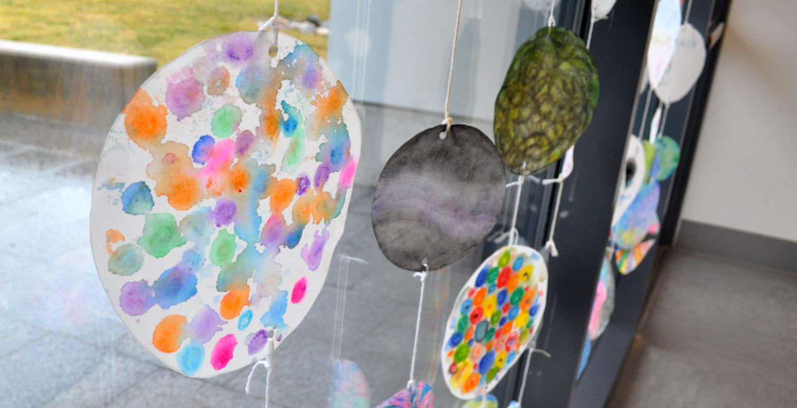 Circular paintings hanging in a window on a rainy day.