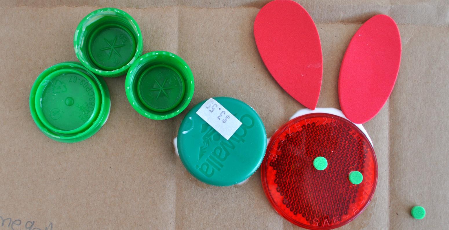 A Very Hungry Caterpillar made from red and green found materials including bottle caps and styrofoam shapes.
