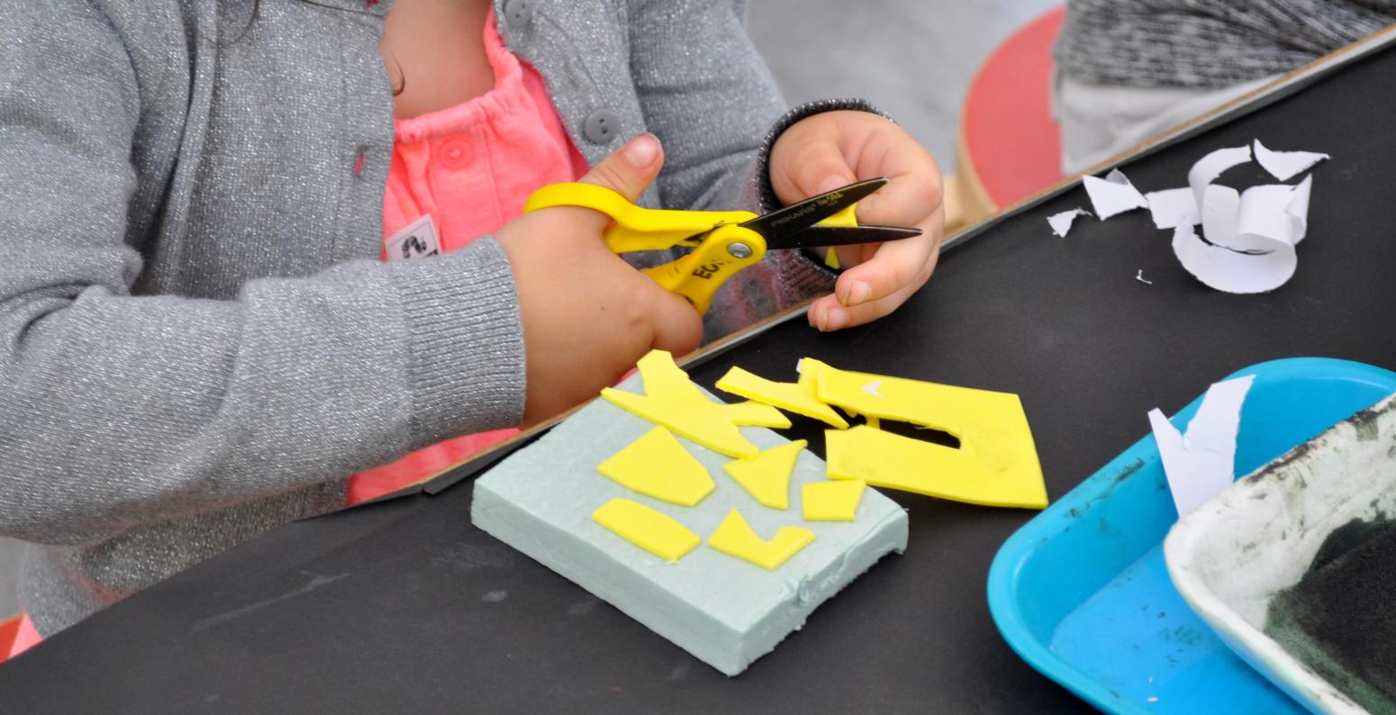A child cuts yellow self-adhesive foam into shapes to add to her stamp base.