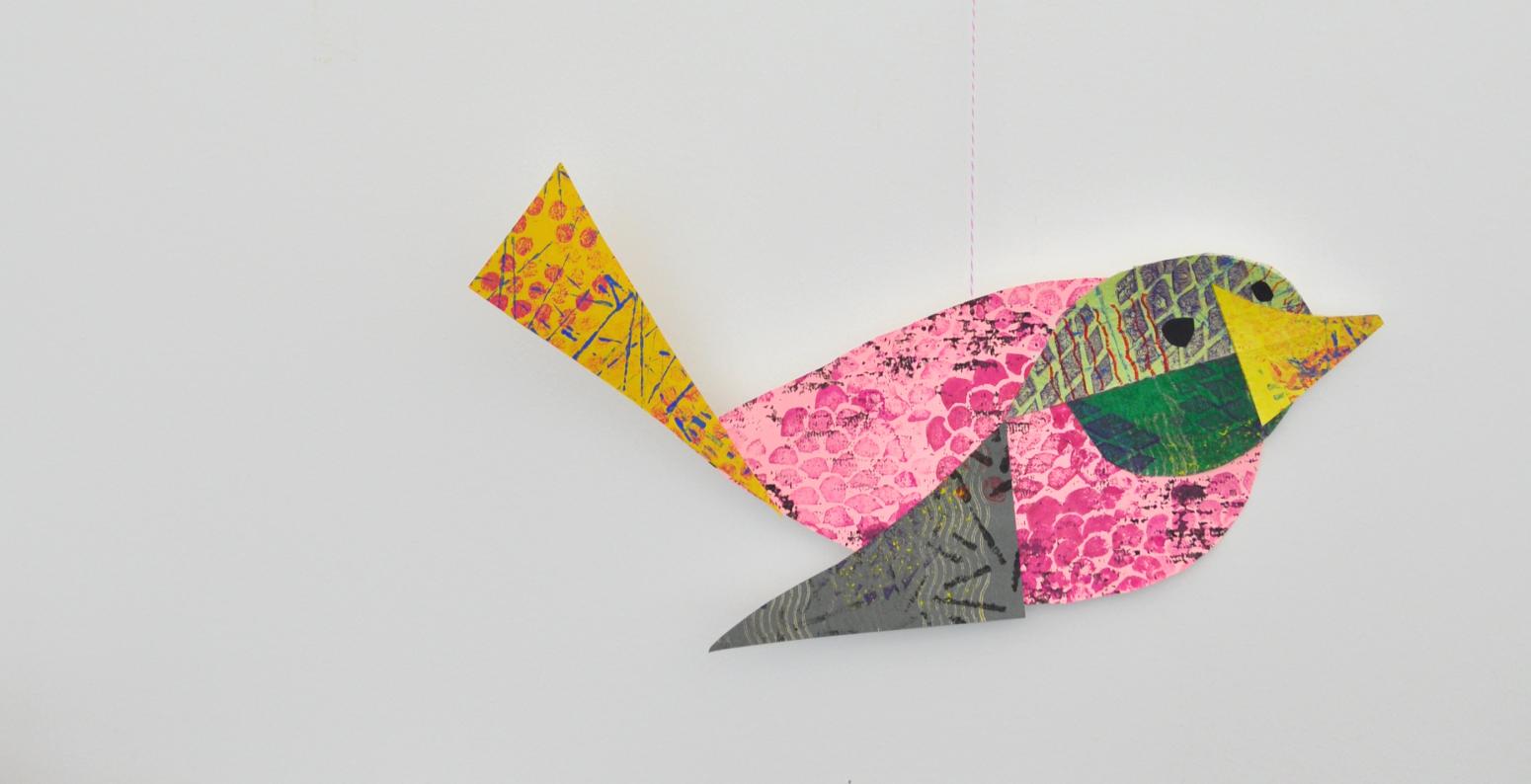 A mobile with one colorful collage bird hanging from a wooden twig.