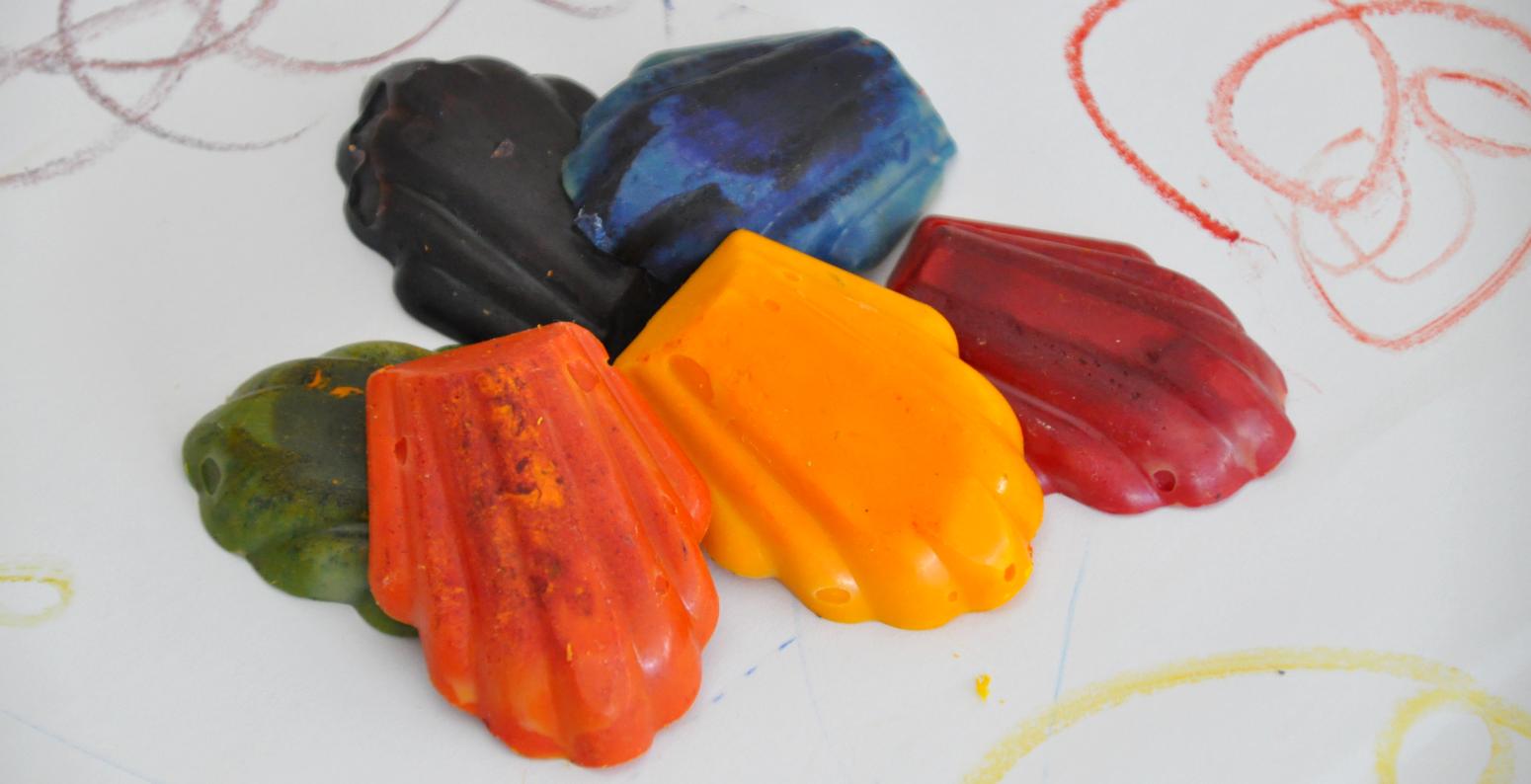 Colorful homemade crayons in the shape of madeleine cookies surrounded by scribbles on white paper.