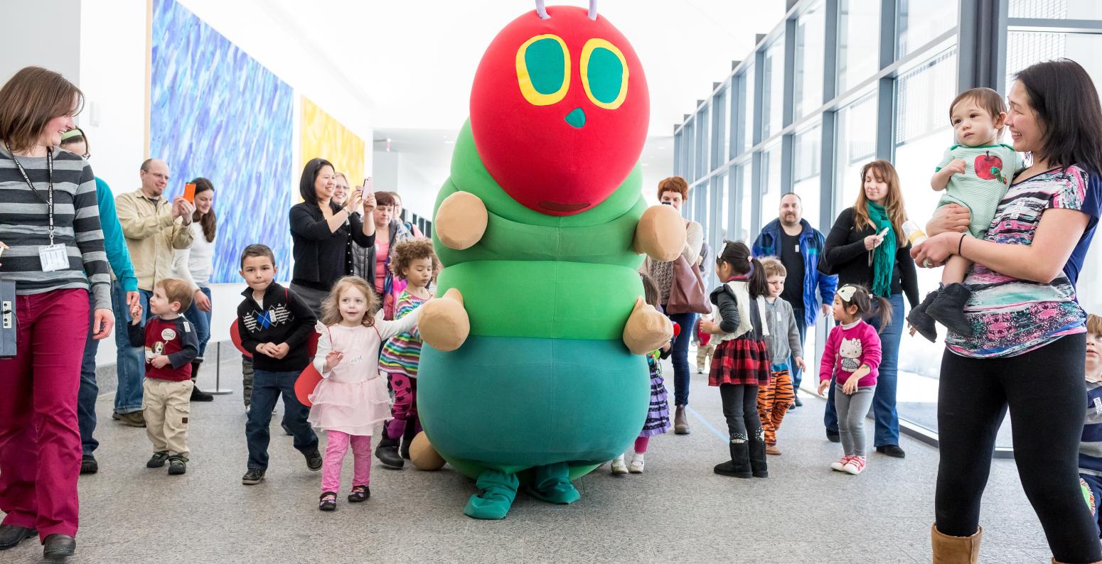 Visitors in the museum walking next to The Very Hungry Caterpillar costume.