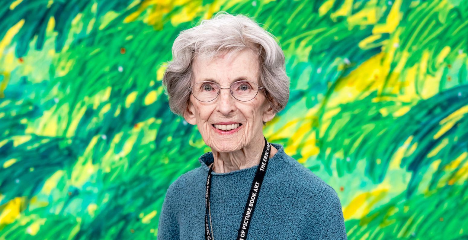 Barbara Elleman stands in front of a green mural by Eric Carle.