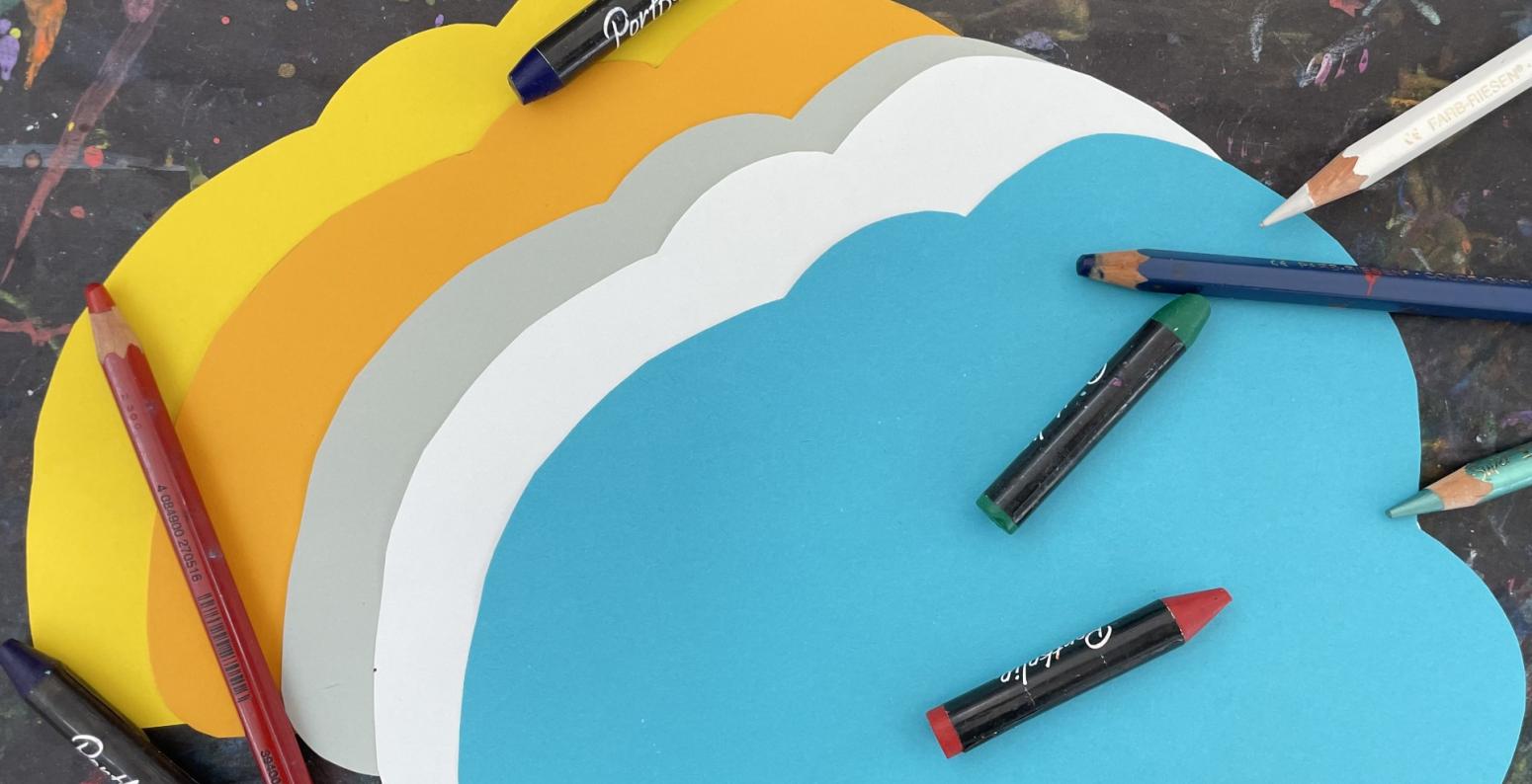 Cloud shaped papers with oil pastels and colored pencils scattered about.