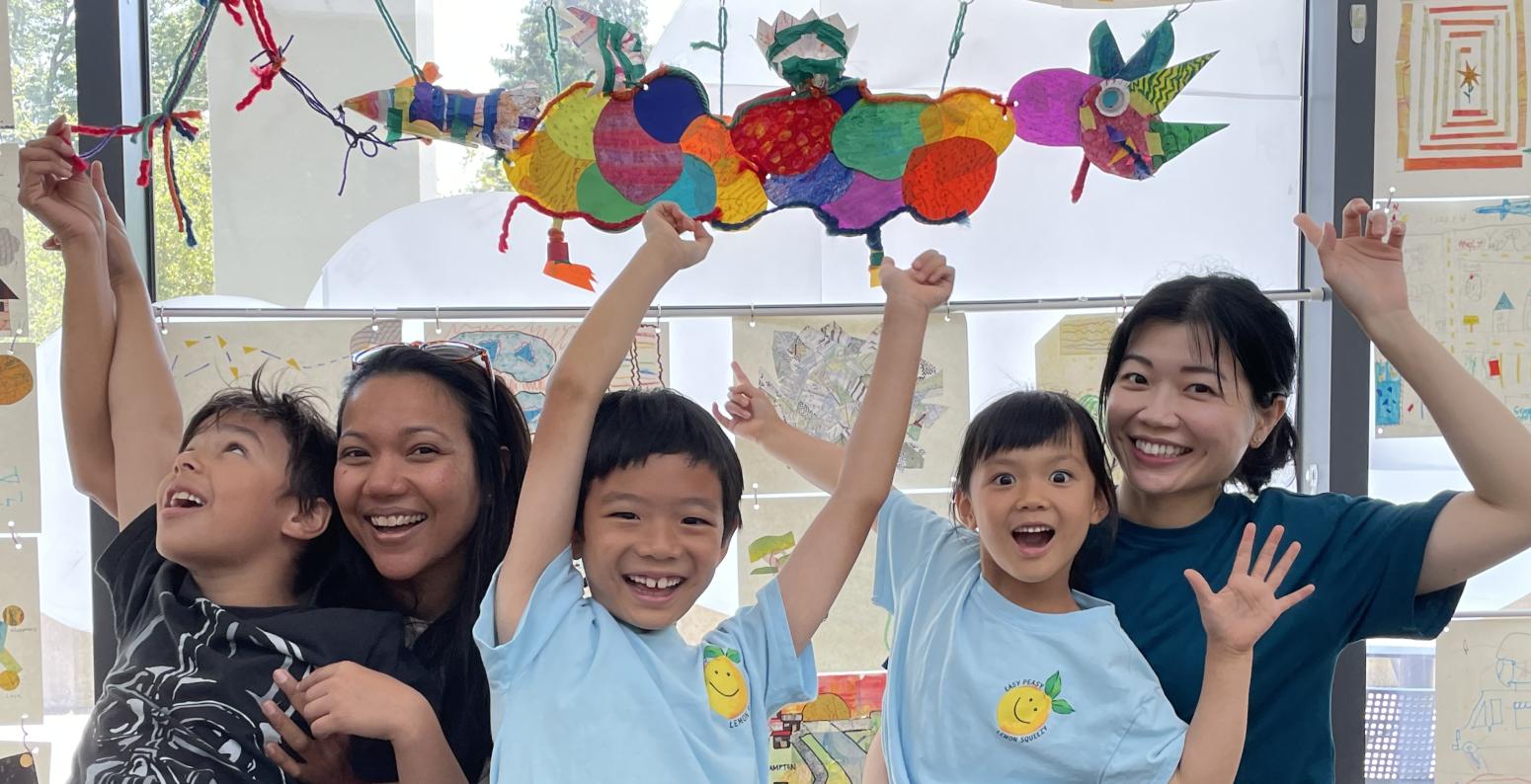 Two adults and three children point above in excitement to their floating paper dragon creation!