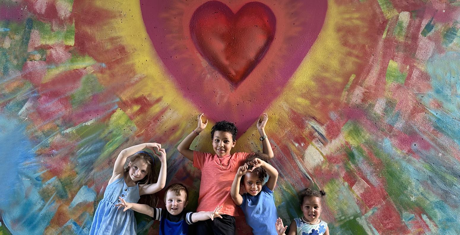 Group of kids smiling in front of heart mural.