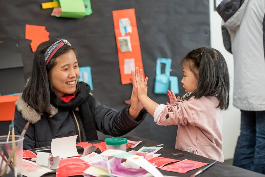 adult and child give high fives while making art in the art studio at The Carle