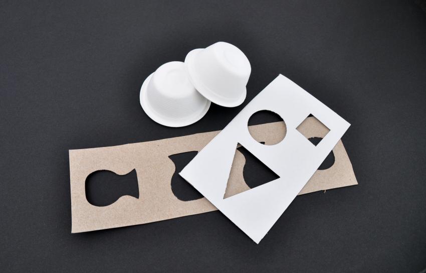 Two small white cups next to two cardboard stencils. 