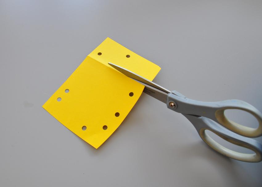 A pair of scissors cutting a used piece of yellow paper, cutting along a fold line.