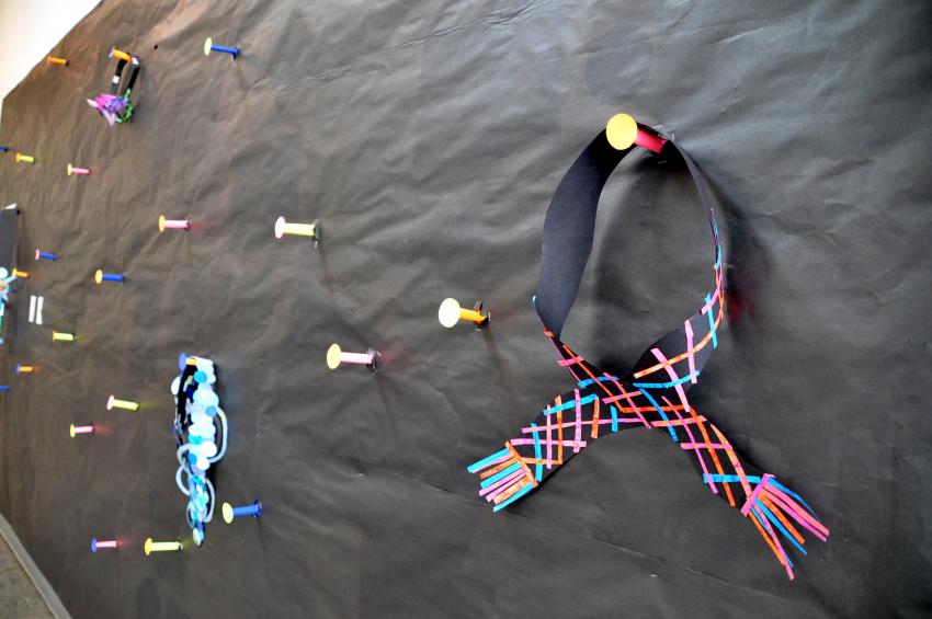 Bulletin board covered with black paper and brightly colored paper pegs.