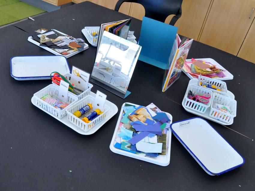 Art Studio table with trays of collage materials, books, and mirrors. 