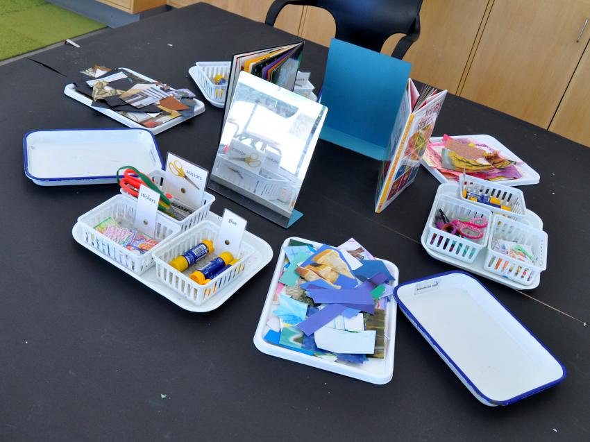 Art Studio table with trays of collage materials, books, and mirrors.
