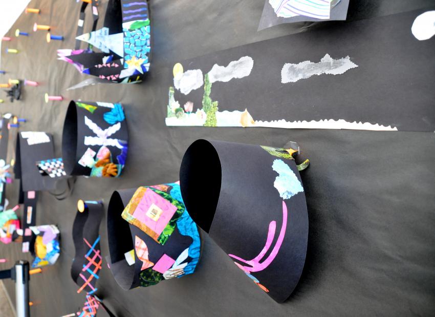 Display wall filled with wearable art pieces hanging on paper pegs.