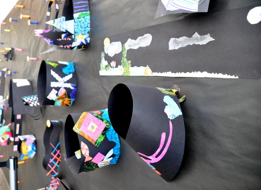 Display wall filled with wearable art pieces hanging on paper pegs. 