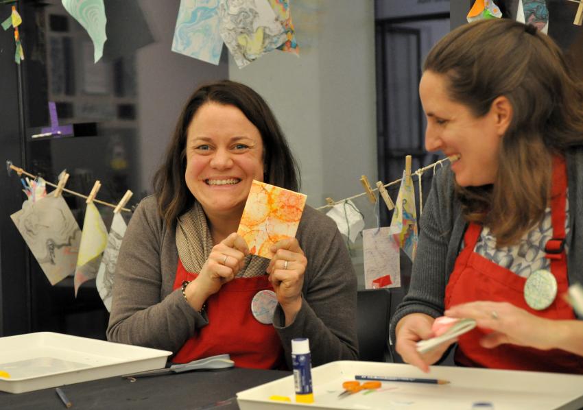 Two participants smiling while one holds up their book covered in marbled paper.