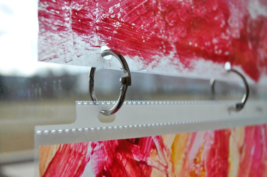 A window display with red, pink, and yellow paintings held together by metal binder rings.