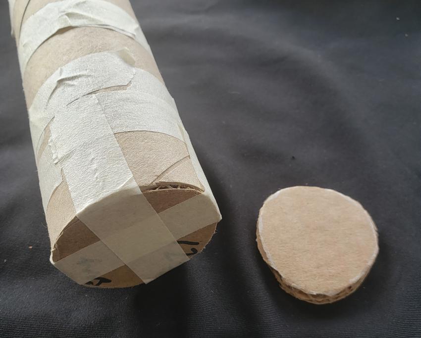 A paper towel roll covered in masking tape with a small round cardboard cutout. 