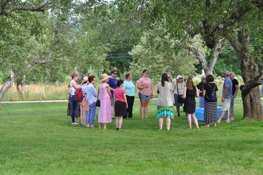 A group of volunteers and staff from The Carle circle around together in the meadow, listening to meadow consultant Owen Wormser.