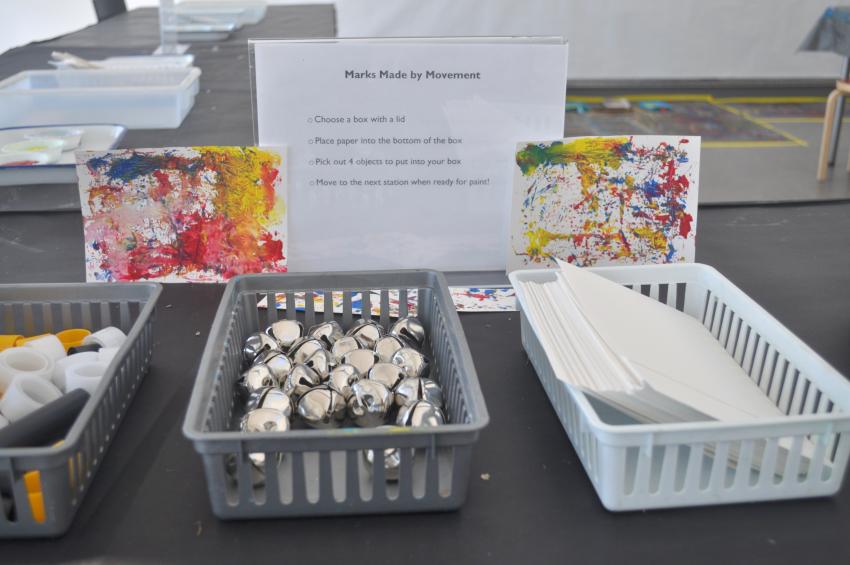 Baskets filled with art supplies in front of two paintings and a sign that says "Marks made by movement." 